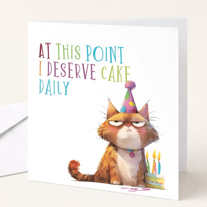 Funny cat birthday card from Whimsi Lilley featuring humorous text about deserving cake daily with a playful cat illustration.