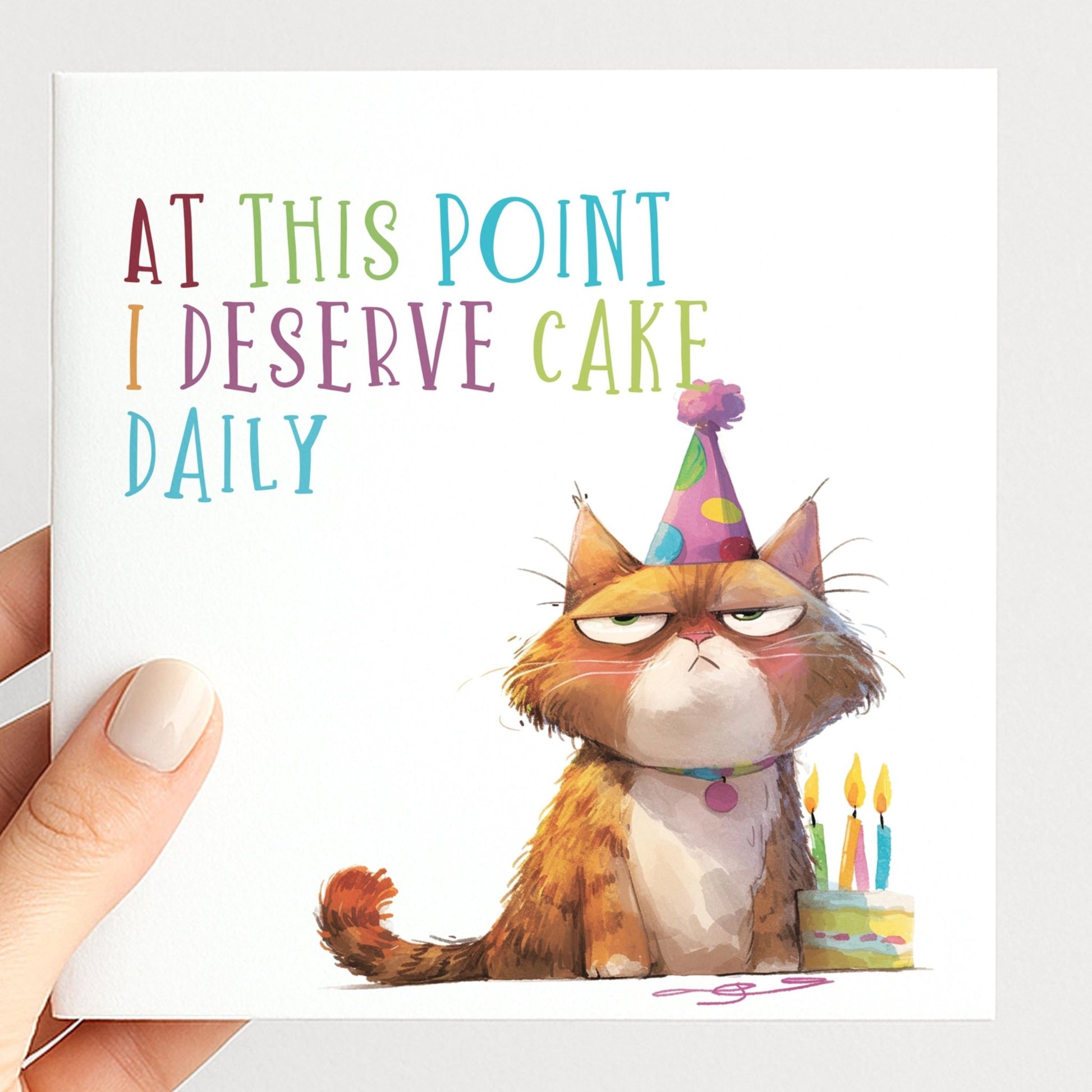Funny Cat Birthday Card by Whimsi Lilley featuring a humorous cat illustration and the phrase "At this point I deserve cake daily."