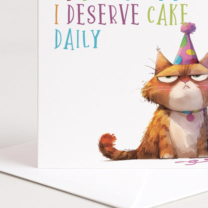 Funny Cat Birthday Card by Whimsi Lilley featuring a humorous illustration and the message "At this point I deserve cake daily."