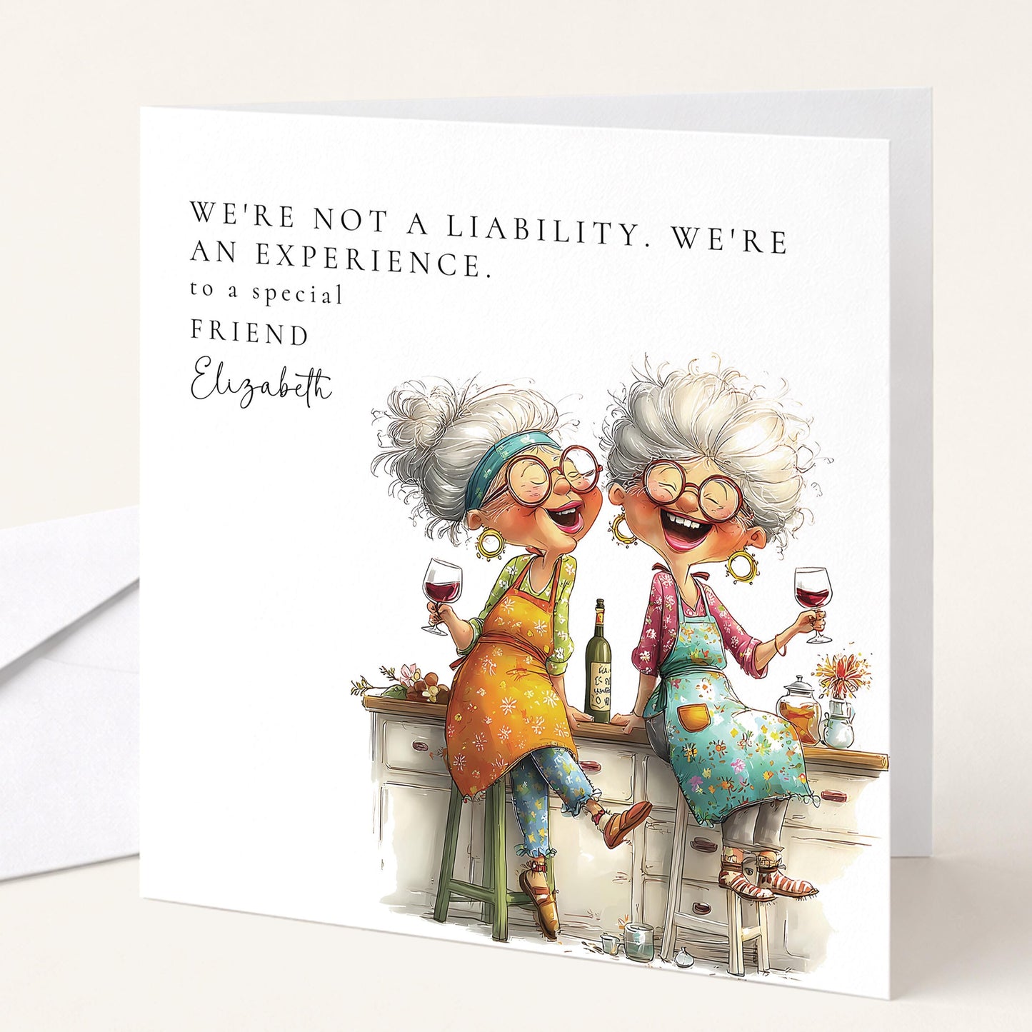 Funny personalised birthday card for friend with two older women laughing over red wine in kitchen captioned Not a Liability An Experience