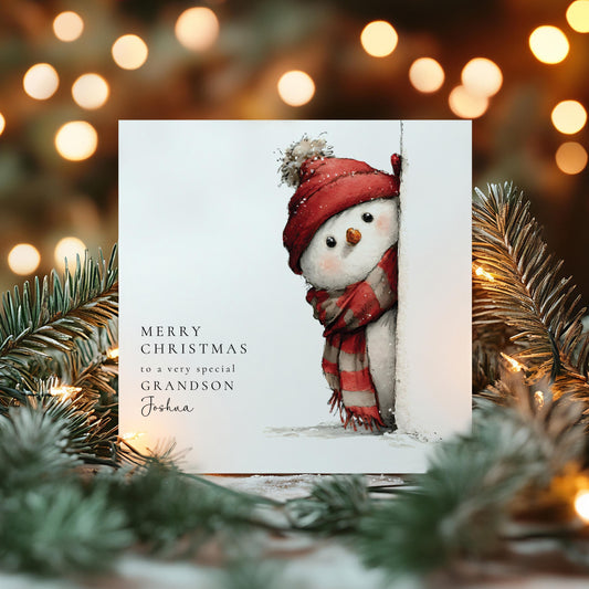 May include: A Christmas card with a watercolour illustration of a snowman wearing a red hat and scarf, peeking from behind a white surface. The card includes the text "MERRY CHRISTMAS to a very special GRANDSON Joshua."