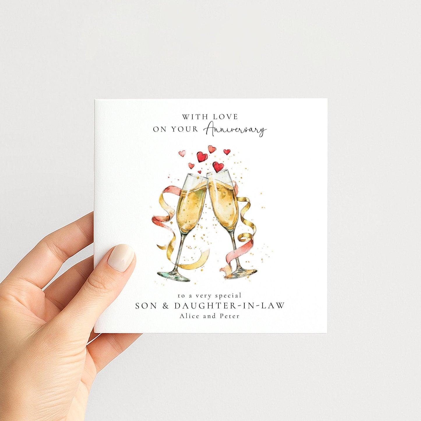 a hand holding a card with a celebratory design featuring champagne glasses and heart-shaped decorations.