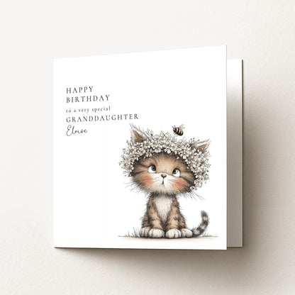 A birthday card featuring a cute cat wearing a flower crown and sitting on the ground.