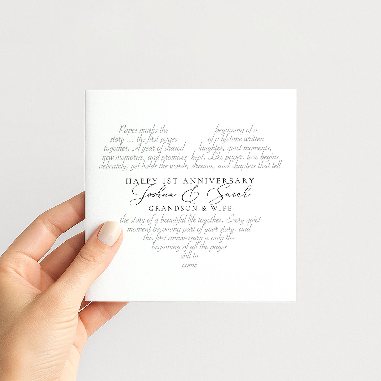 a hand holding a white card with text on it. The card appears to be a wedding invitation or anniversary card, with the text celebrating the first anniversary of a couple named Joshua and Sarah.
