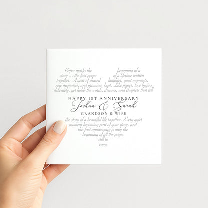 a hand holding a white card with text on it. The card appears to be a wedding invitation or anniversary card, with the text celebrating the first anniversary of a couple named Joshua and Sarah.