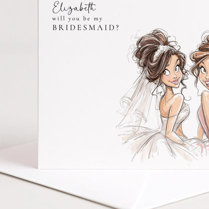 Brunette bride holding a "Will You Be My Bridesmaid" card from Whimsi Lilley, with floral decorations and elegant handwritten style.